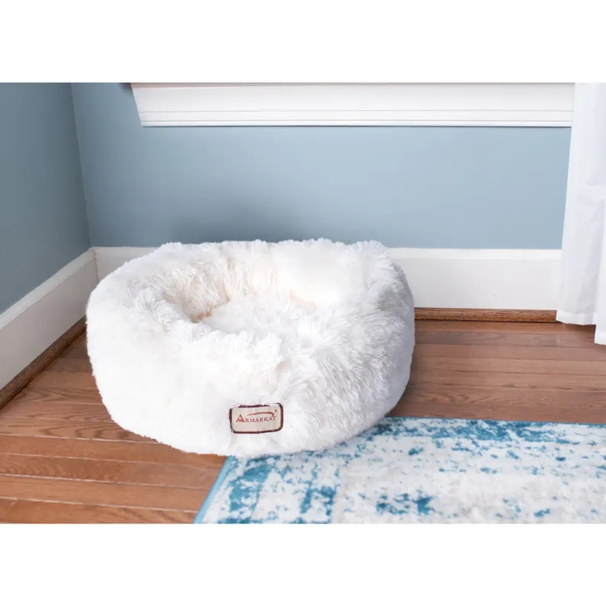 White fluffy pet bed on a wooden floor with a blue rug