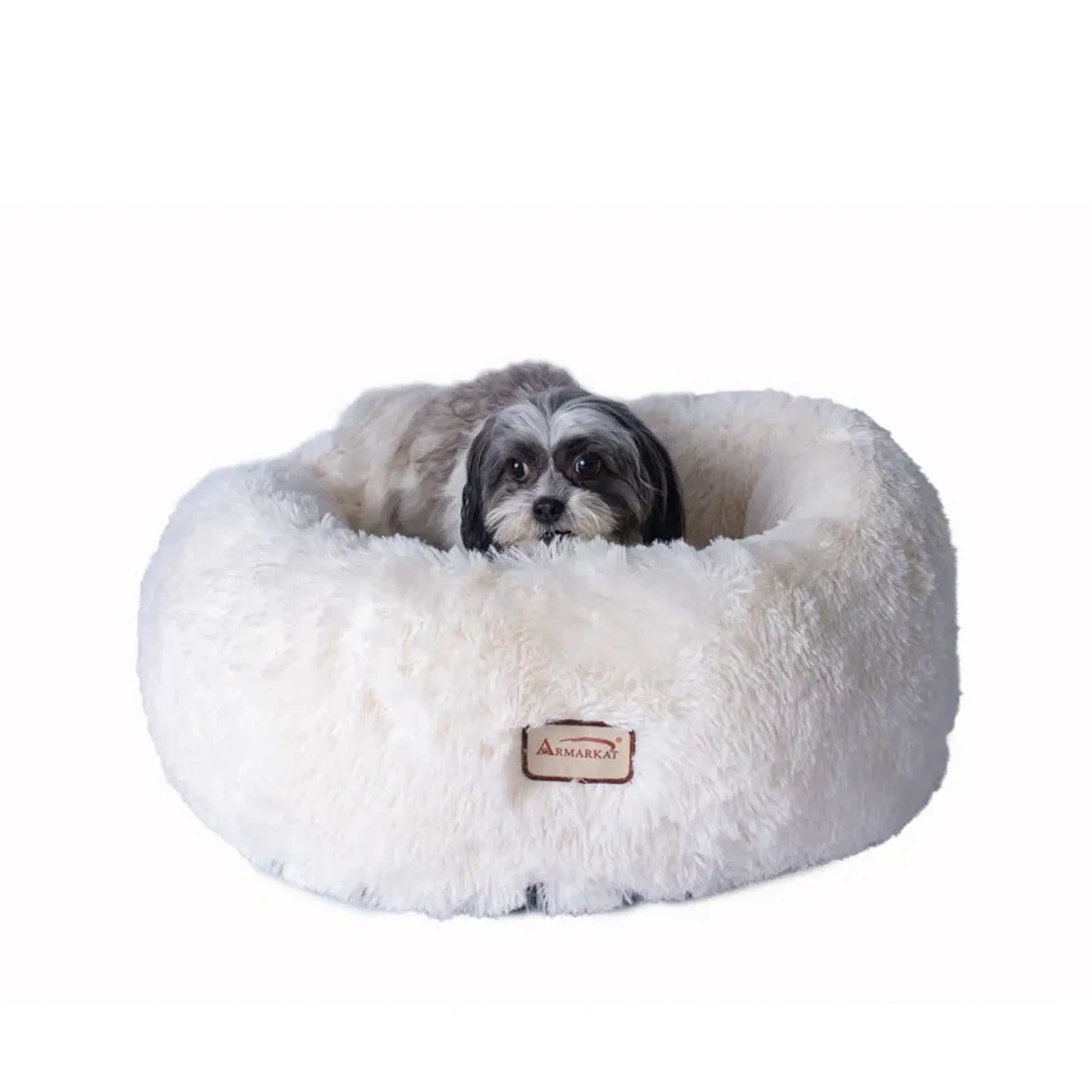 Dog lying on a fluffy white donut bed with a visible brand logo on a white background