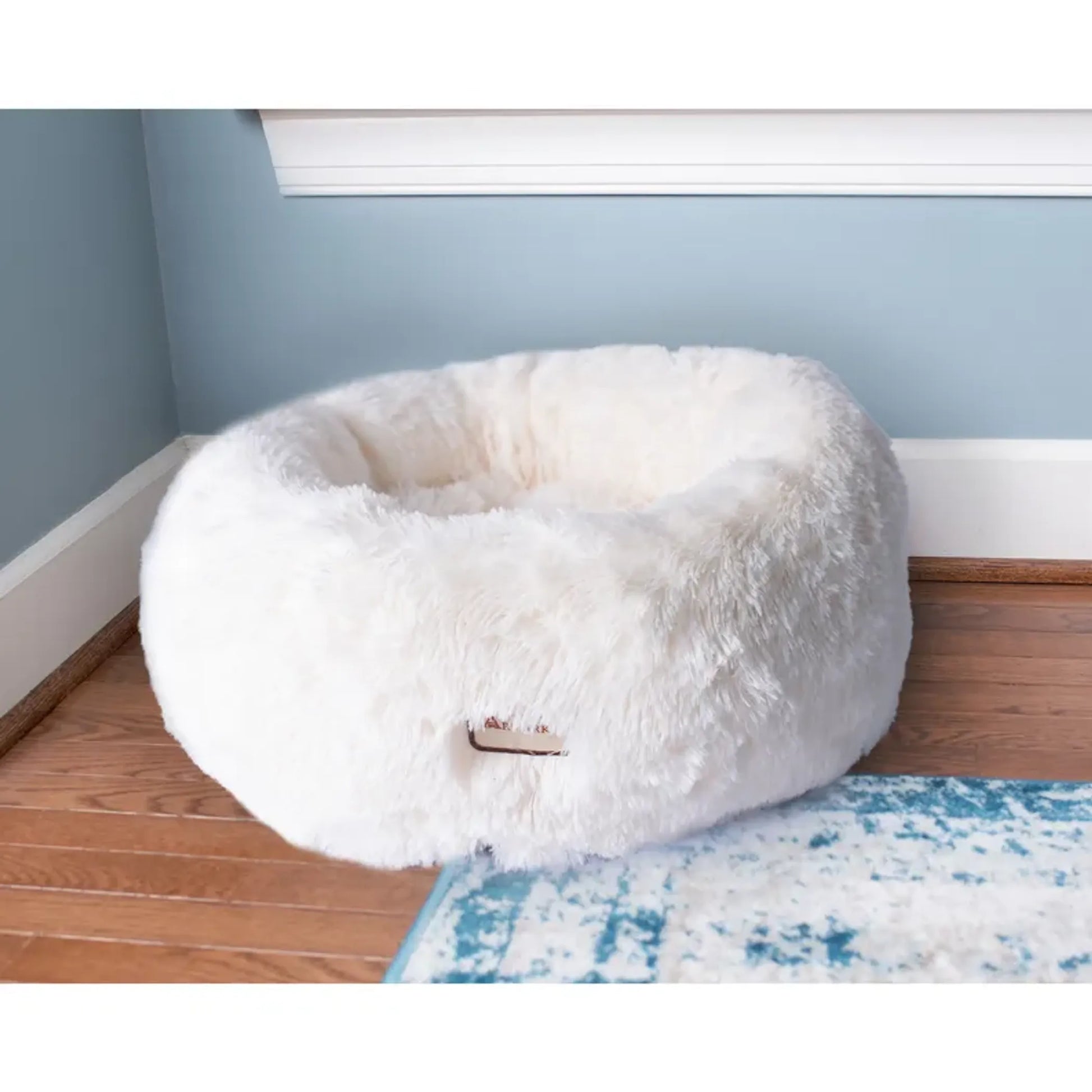 White fluffy pet bed on a wooden floor with a light blue wall in the background