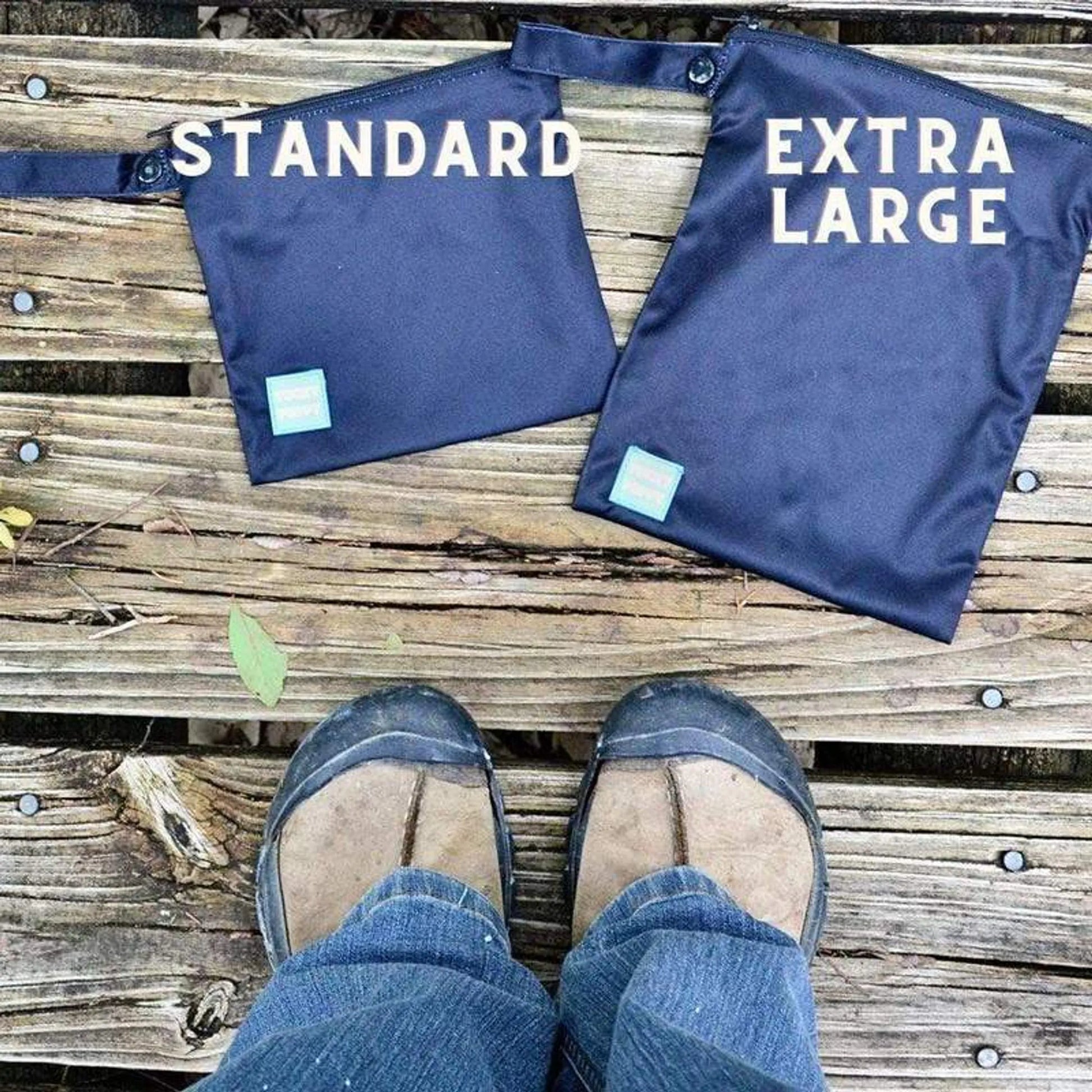 Two navy blue bags labeled 'Standard' and 'Extra Large' on a wooden surface, with a person wearing sandals and jeans.